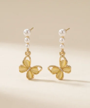 Gold plated butterfly drop earrings with yellow cat-eye stone wings and triple pearl stem on cream background