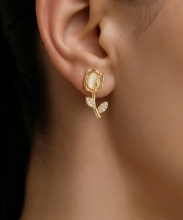 Gold plated tulip dangler earring with mother of pearl bud and CZ pavé leaf stem worn on ear, lifestyle close-up