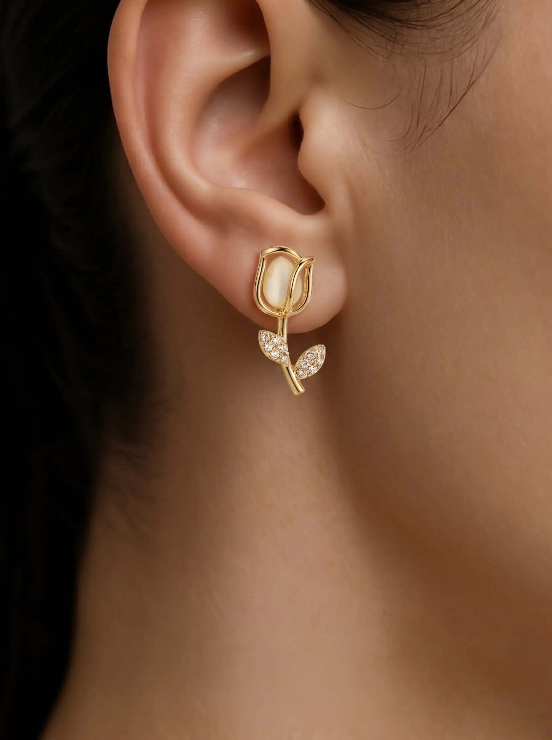 Gold plated tulip dangler earring with mother of pearl bud and CZ pavé leaf stem worn on ear, lifestyle close-up