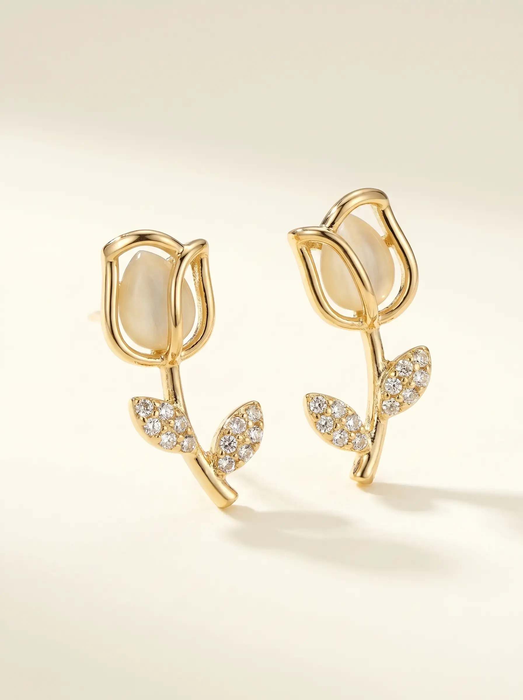 Gold plated tulip dangler earring with mother of pearl bud and CZ pavé leaf stem worn on ear, lifestyle close-up