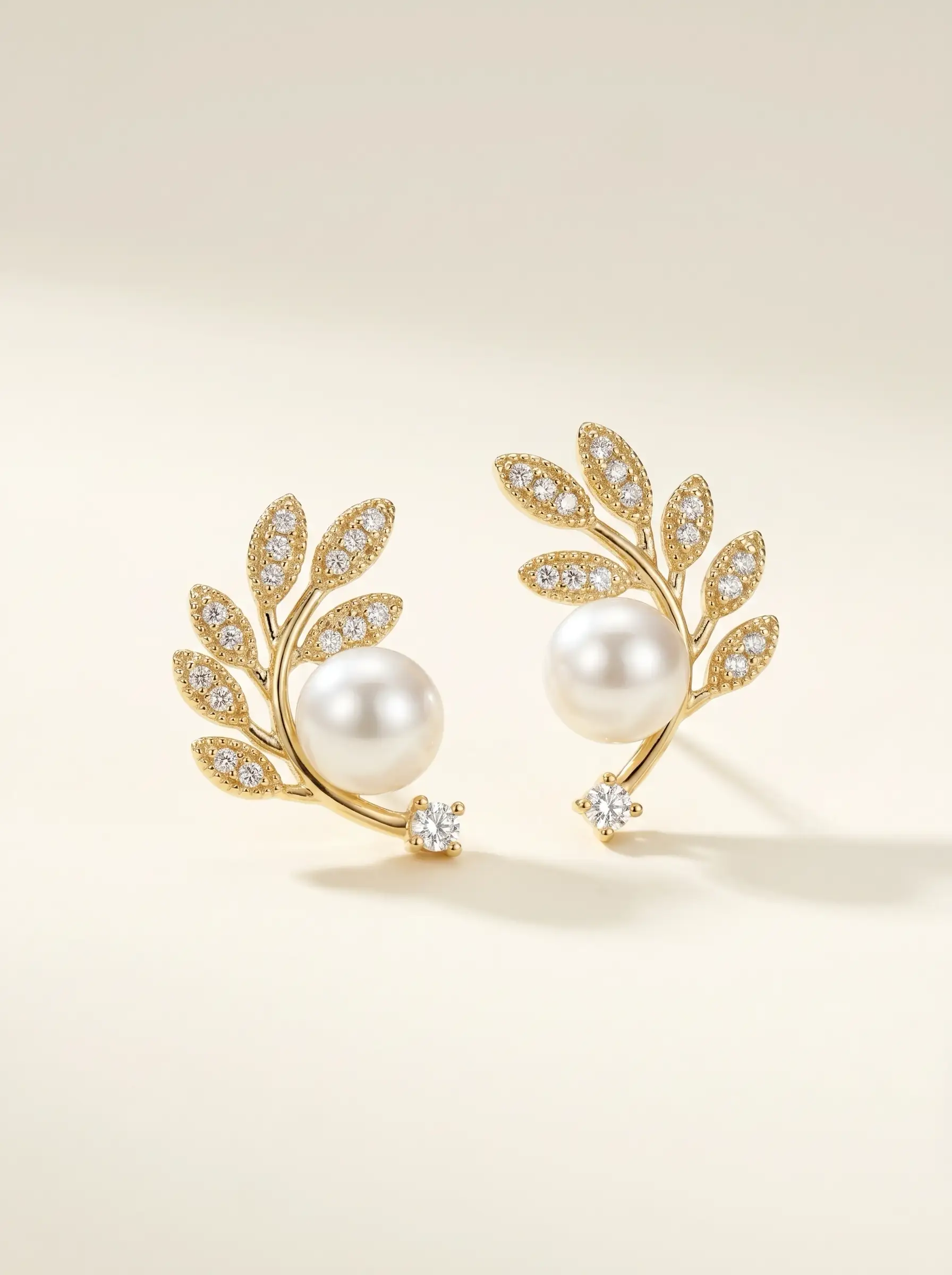 Gold plated olive branch stud earrings with CZ pavé leaves, centred pearl and solitaire CZ tip, studio product pair shot