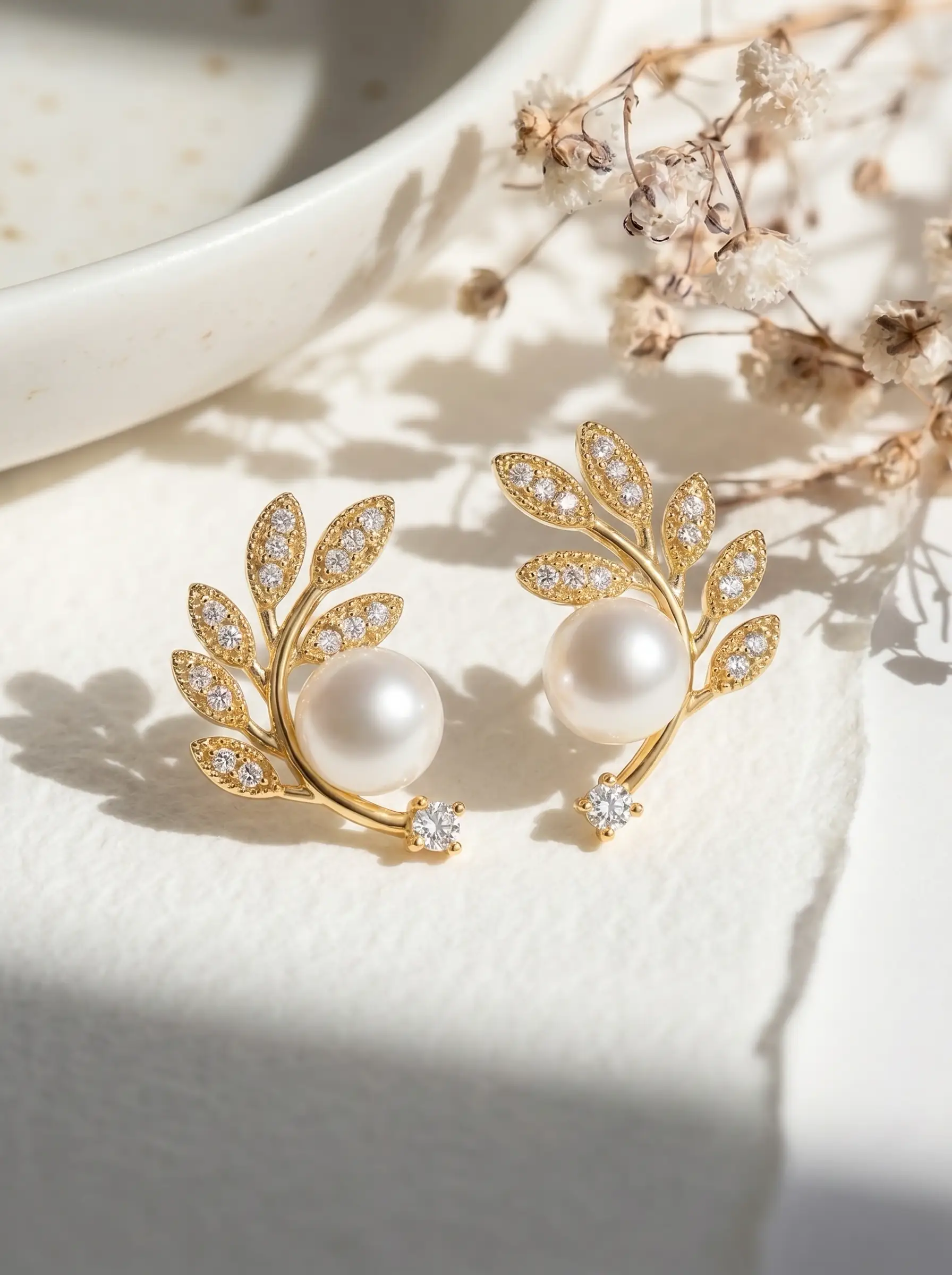 Gold plated olive branch stud earrings with CZ pavé leaves, centred pearl and solitaire CZ tip, studio product pair shot