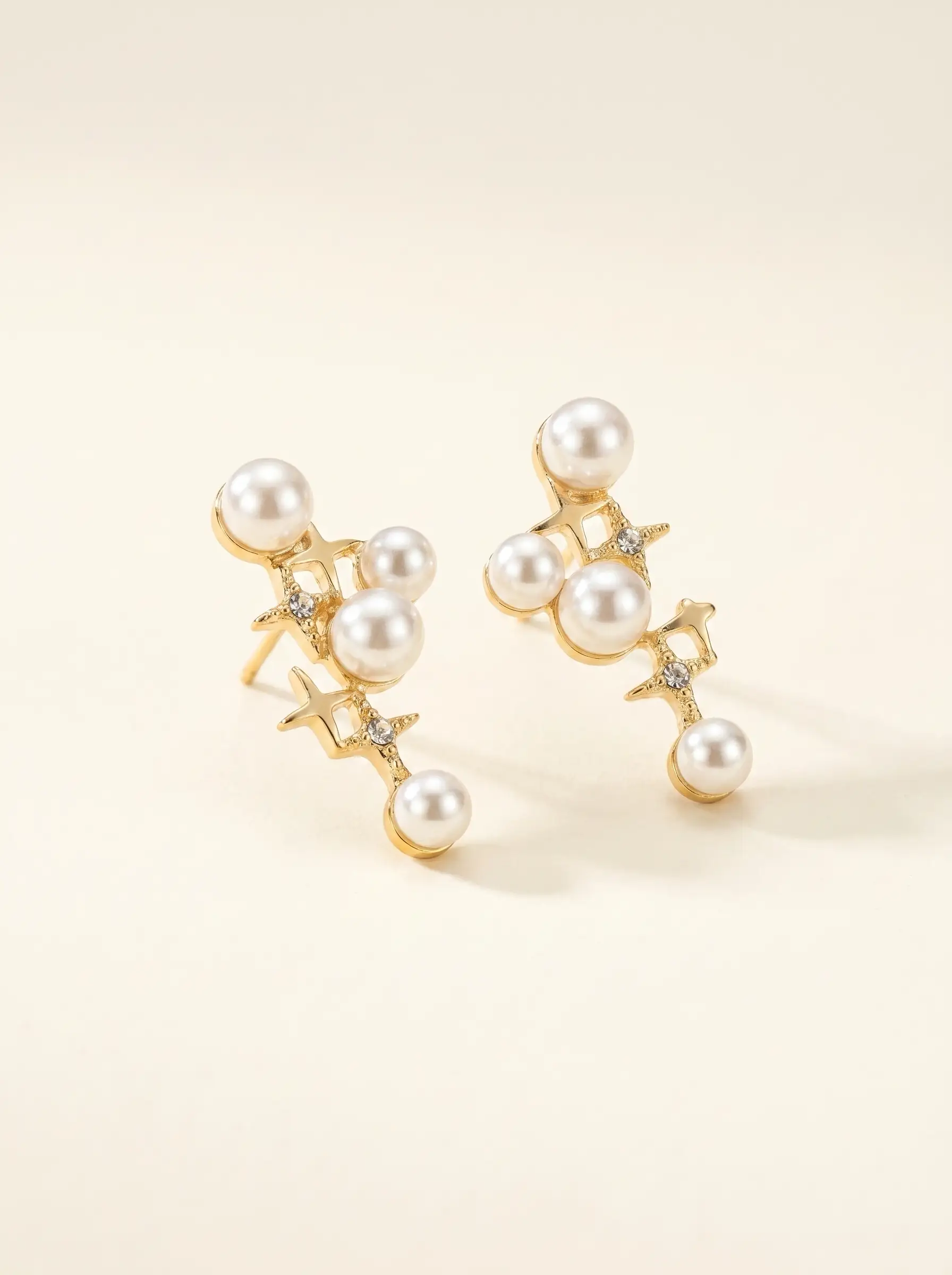 Gold plated cascading pearl drop earrings with four-pointed star CZ connectors, five pearl cluster design, studio product pair shot