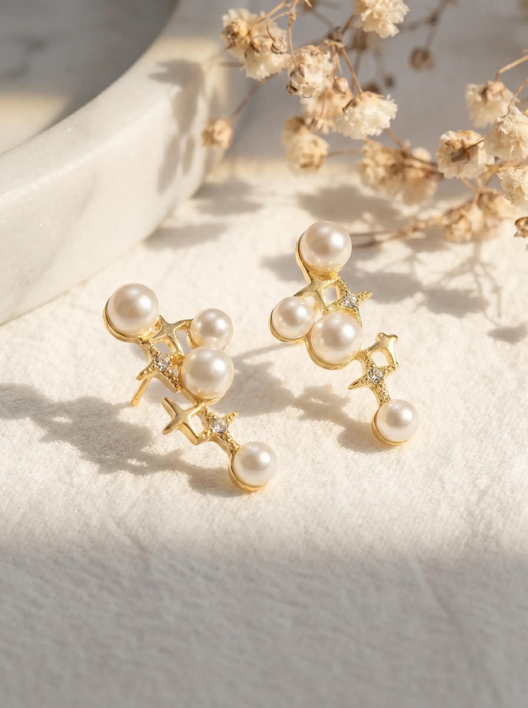 Gold plated cascading pearl drop earrings with four-pointed star CZ connectors, five pearl cluster design, studio product pair shot