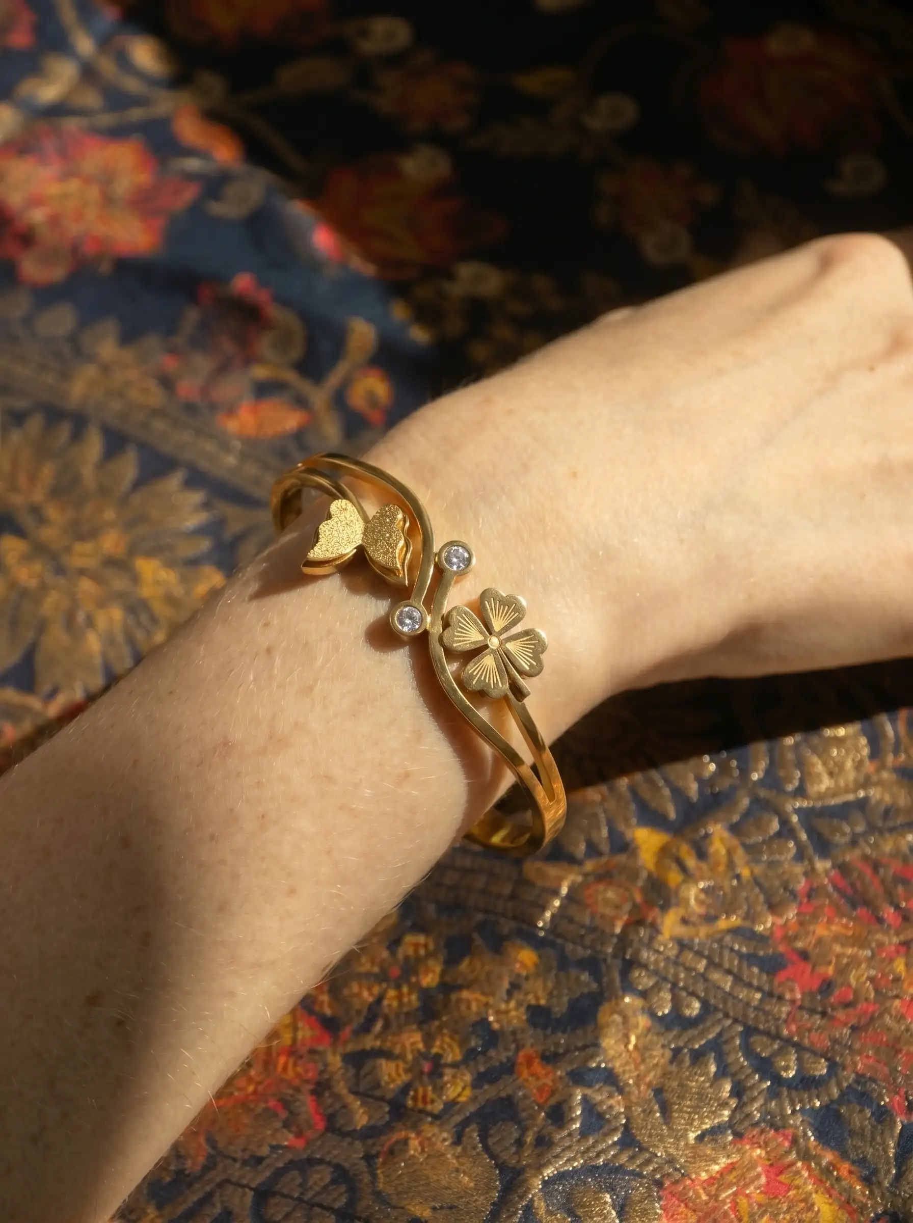 Gold plated bracelet with floral charm and butterfly detail on structured band for women