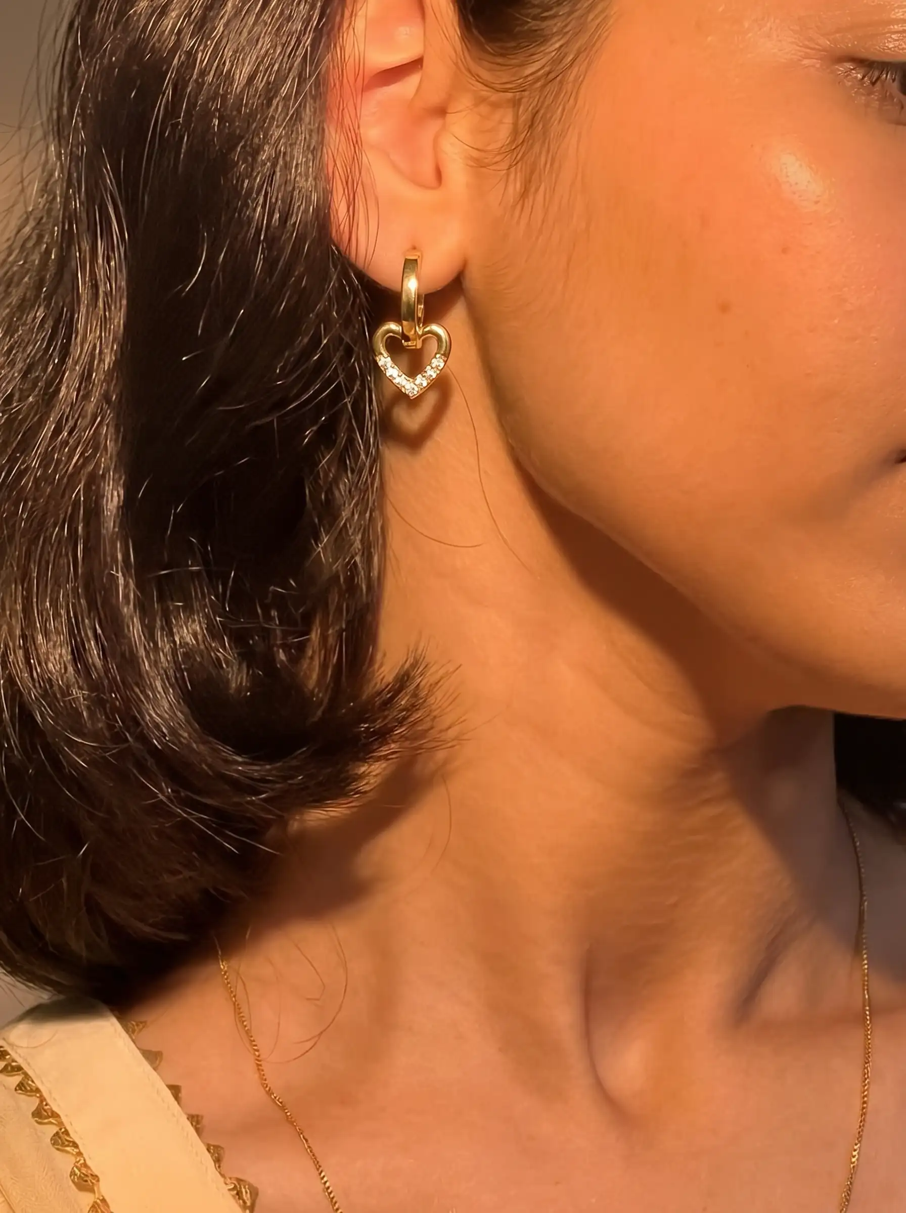 Close-up of gold plated heart drop hoop earrings with crystal detailing for women
